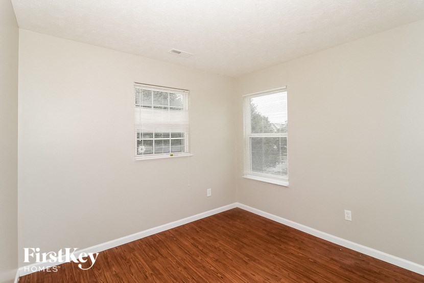 a bedroom with wood floors and two windows