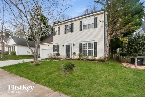 A house with a white exterior and a black roof is surrounded by a green lawn and trees.