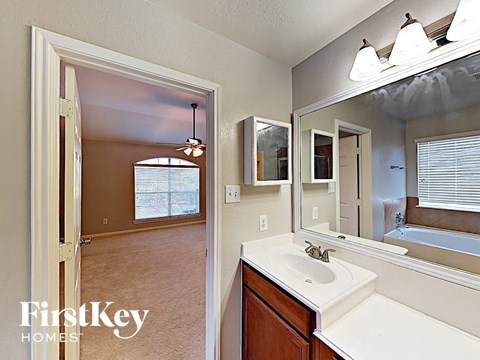 a bathroom with a sink and a mirror and a door to a bedroom