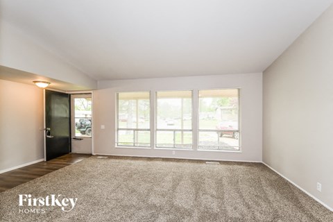 A spacious empty room with a carpeted floor and a door leading to a balcony.