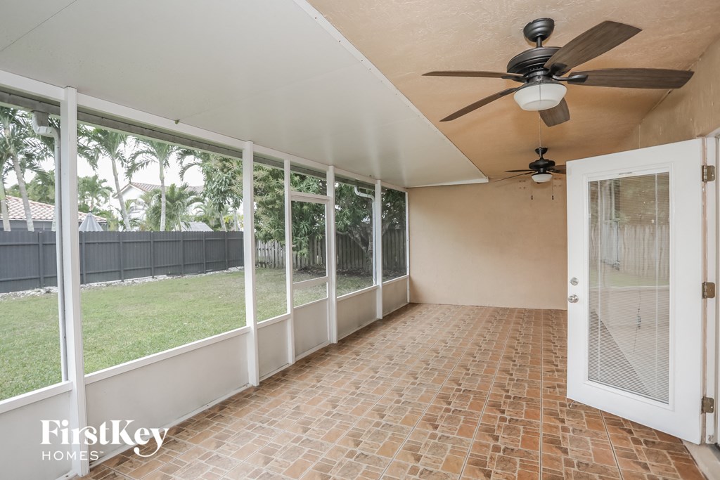 an empty porch with a door to the yard and a ceiling fan