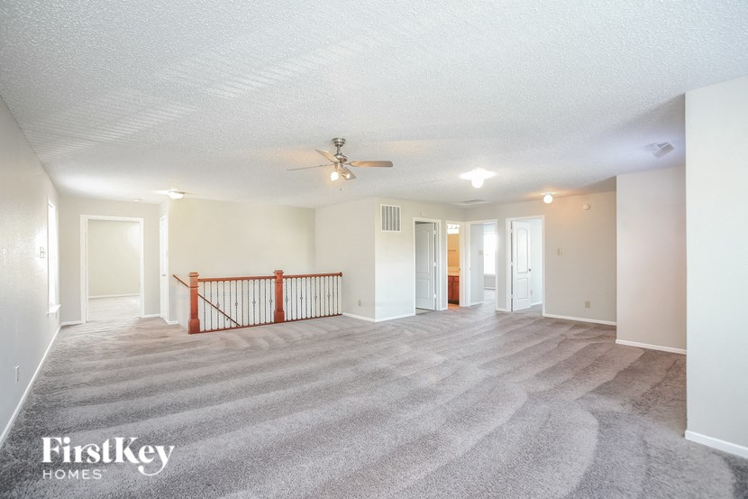an empty living room with a ceiling fan and a carpeted staircase