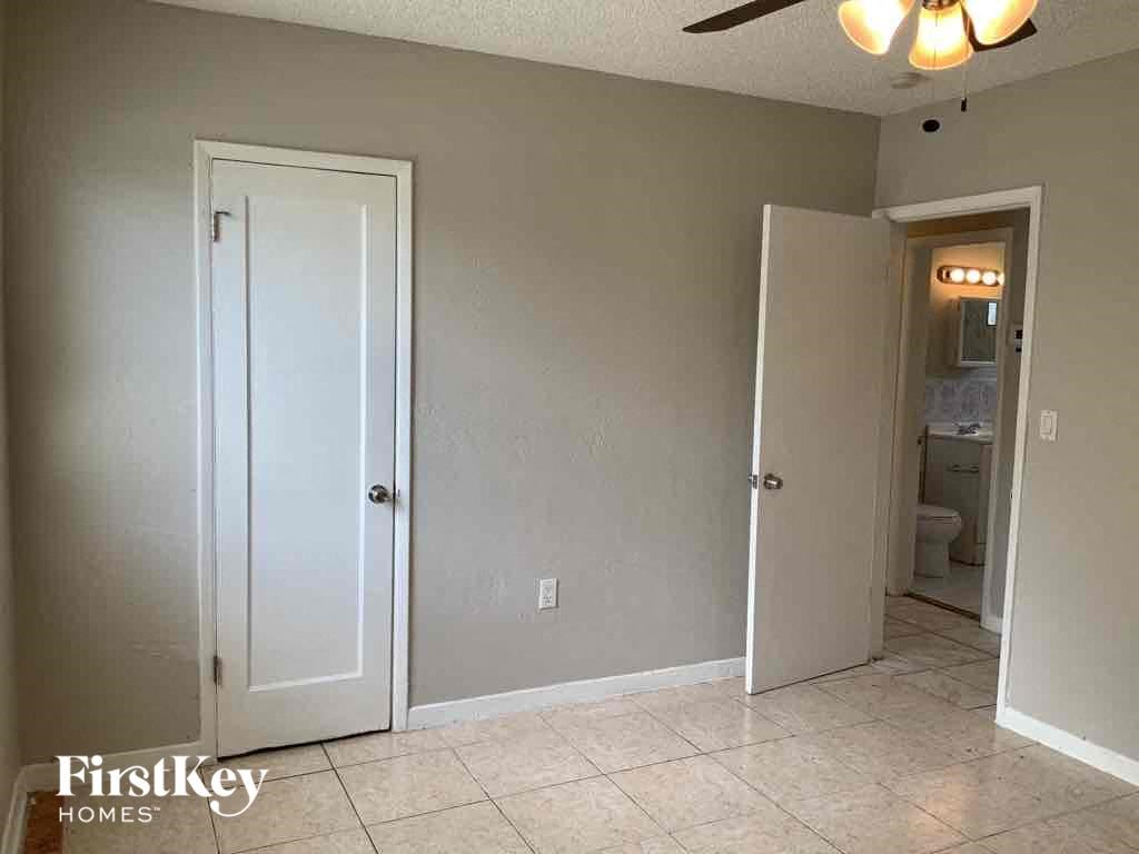 A room with a white door and a bathroom visible through the door.