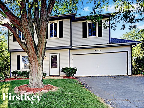A two-story house with a garage and a tree in front.