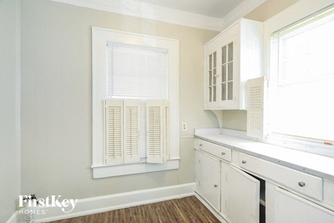 A kitchen with white cabinets and a window with blinds.