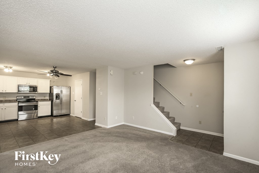 an empty living room with a kitchen and a ceiling fan