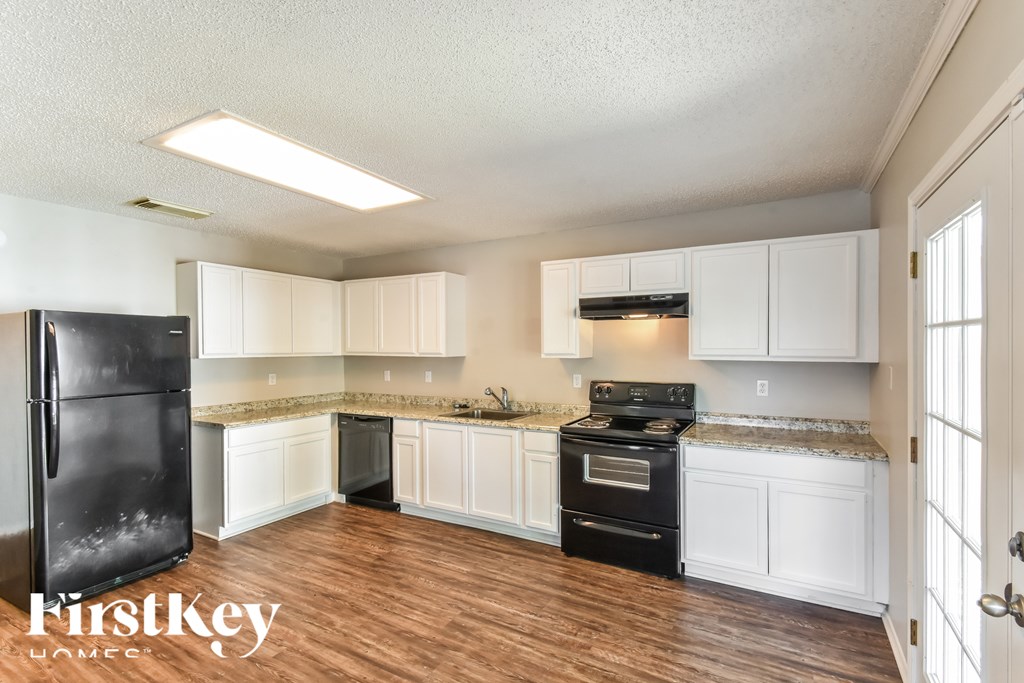 A kitchen with white cabinets and a black fridge.