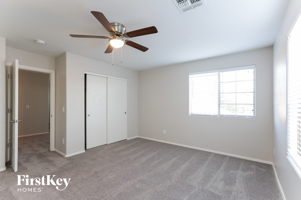 A spacious room with a ceiling fan and a window with blinds.
