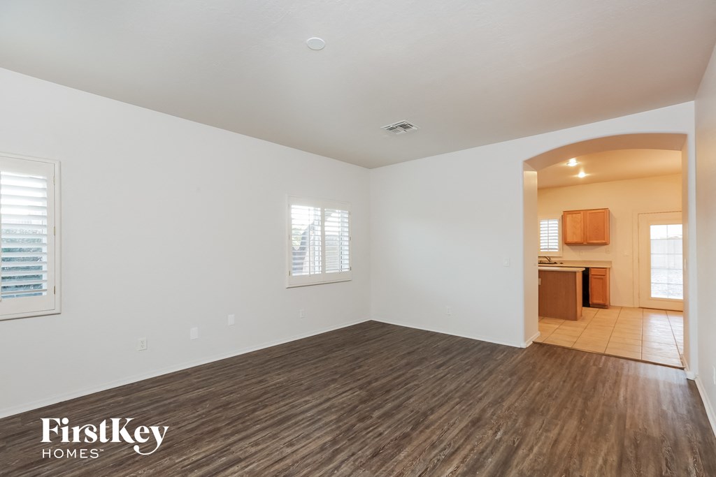 an empty living room with a kitchen in the background