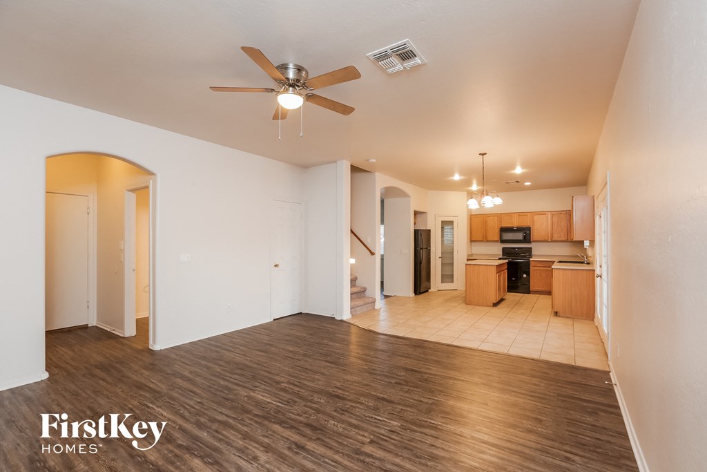 an empty living room with a ceiling fan and a kitchen