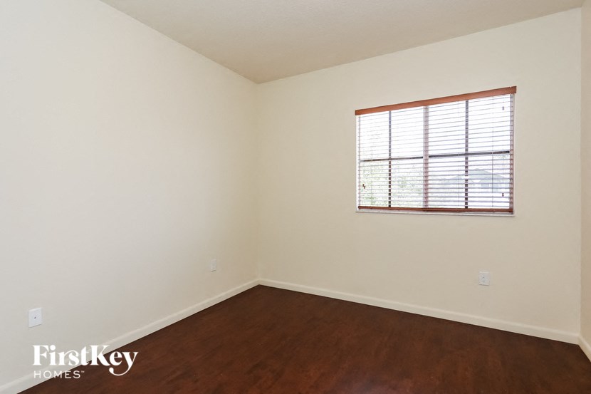 a bedroom with white walls and wood floors and a window