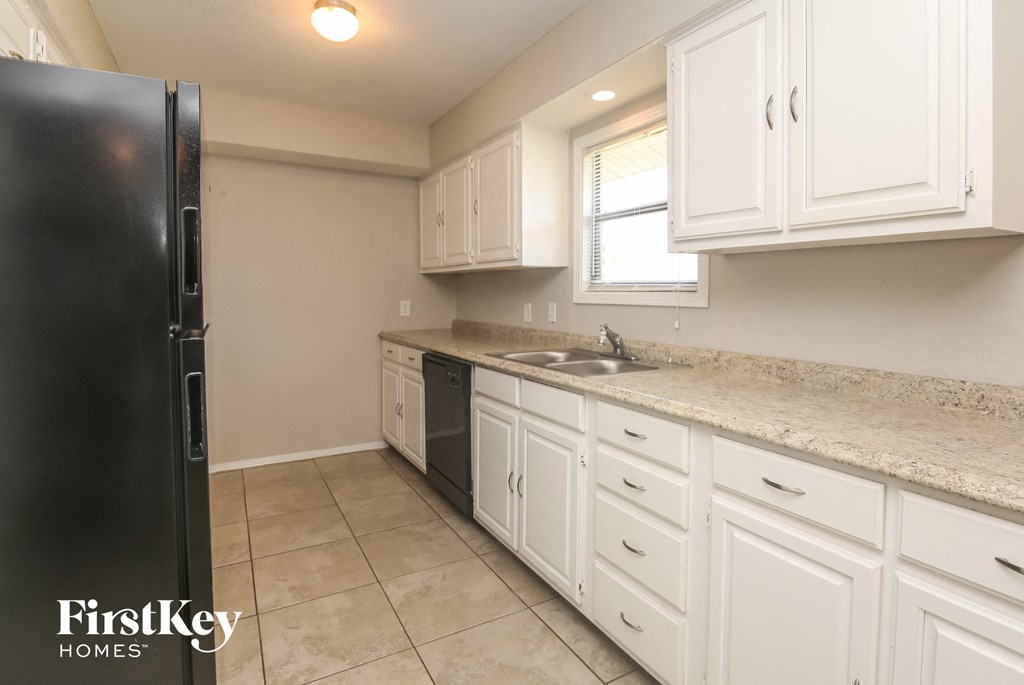 A kitchen with white cabinets and a black refrigerator.