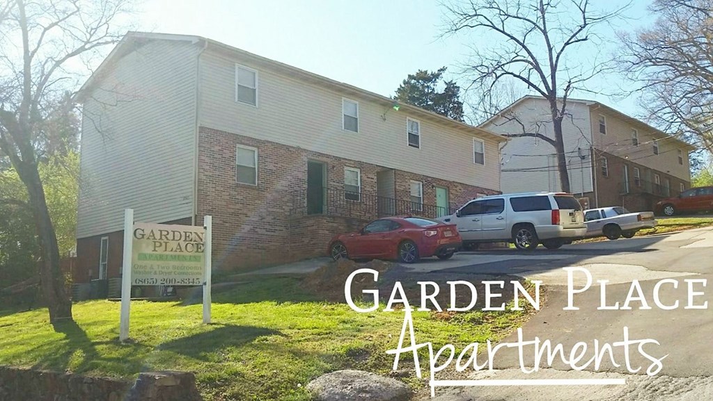 A sign for Garden Place Apartments is in front of a building with cars parked in front.