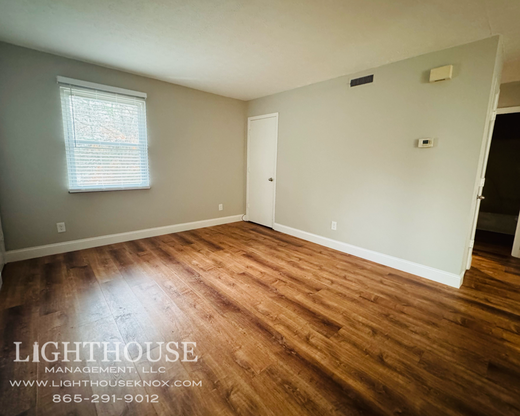 A room with wooden flooring and a window with blinds.
