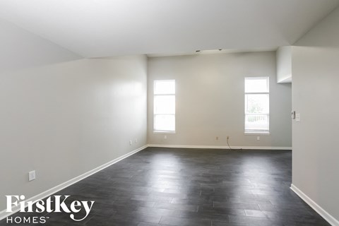 A spacious room with black flooring and two windows.