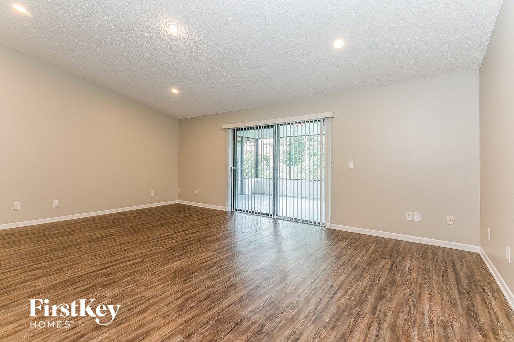 A spacious room with wooden flooring and a sliding glass door leading to a balcony.
