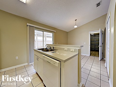 A kitchen with a white counter top and a window with blinds.