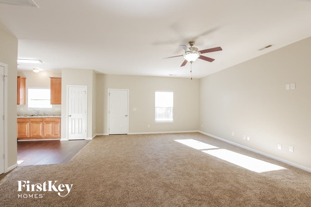 an empty living room with a ceiling fan and a kitchen