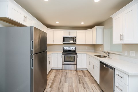 A kitchen with a refrigerator on the left and a microwave, oven, and sink in the middle.