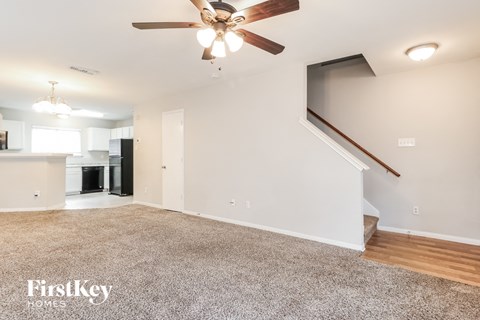 A spacious living room with a carpeted floor and a ceiling fan.