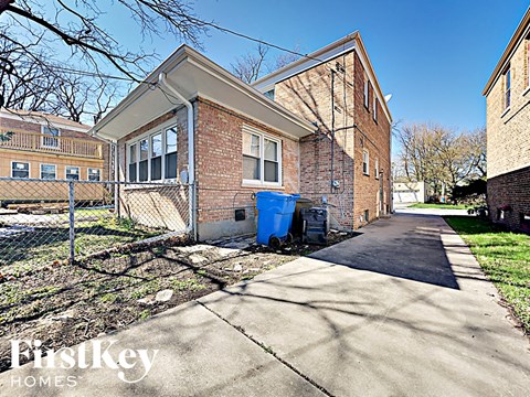the front of a brick building with a sidewalk and a trash can