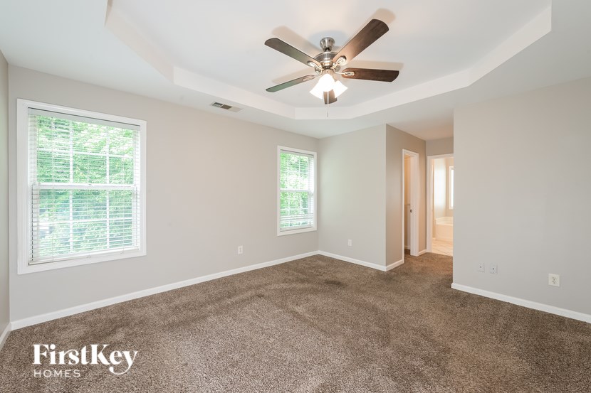 A spacious room with a ceiling fan and two windows.