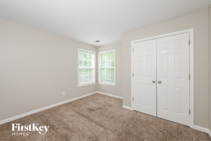 A room with a carpeted floor, a white door, and a window with blinds.