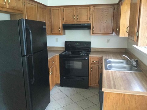 A black refrigerator stands in a kitchen with wooden cabinets.
