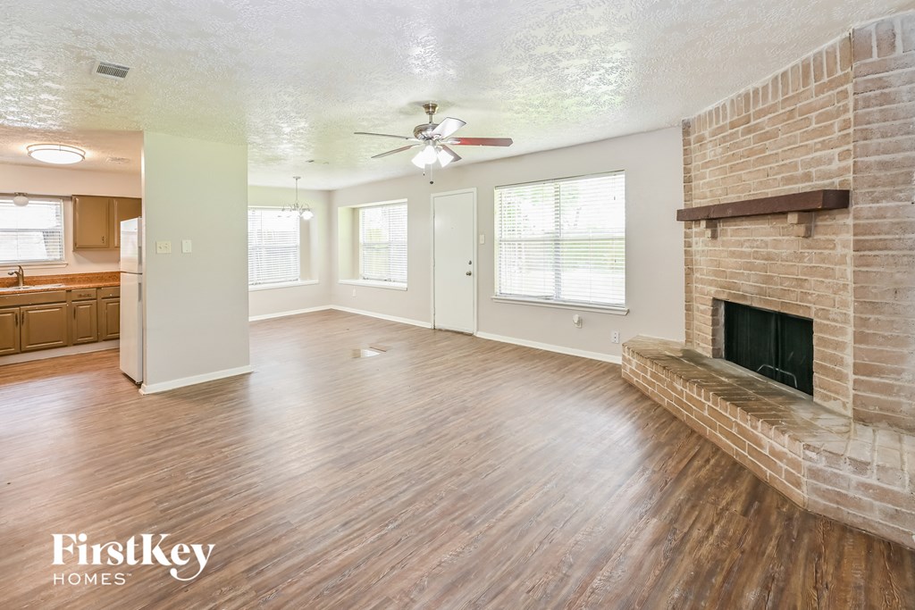 an empty living room with a brick fireplace and a ceiling fan