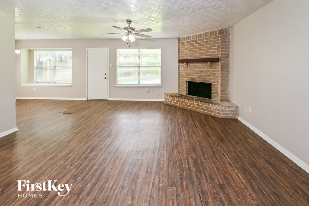 an empty living room with a brick fireplace and wooden floors