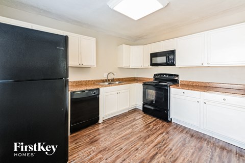 A black refrigerator is in a kitchen with wooden floors and white cabinets.