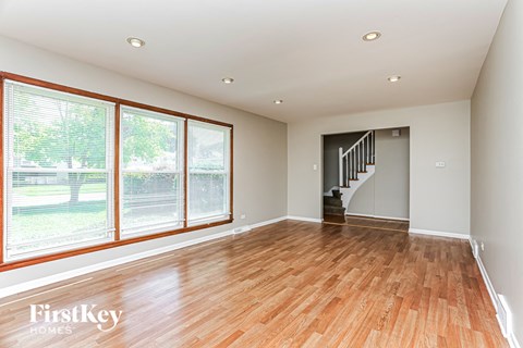 A spacious room with wooden floors and a staircase.