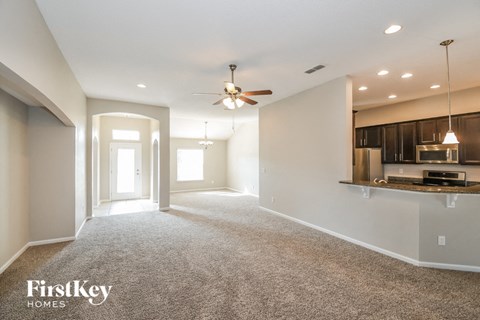 an empty living room with a ceiling fan and a kitchen