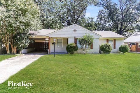 A white house with a garage is surrounded by green grass and trees.