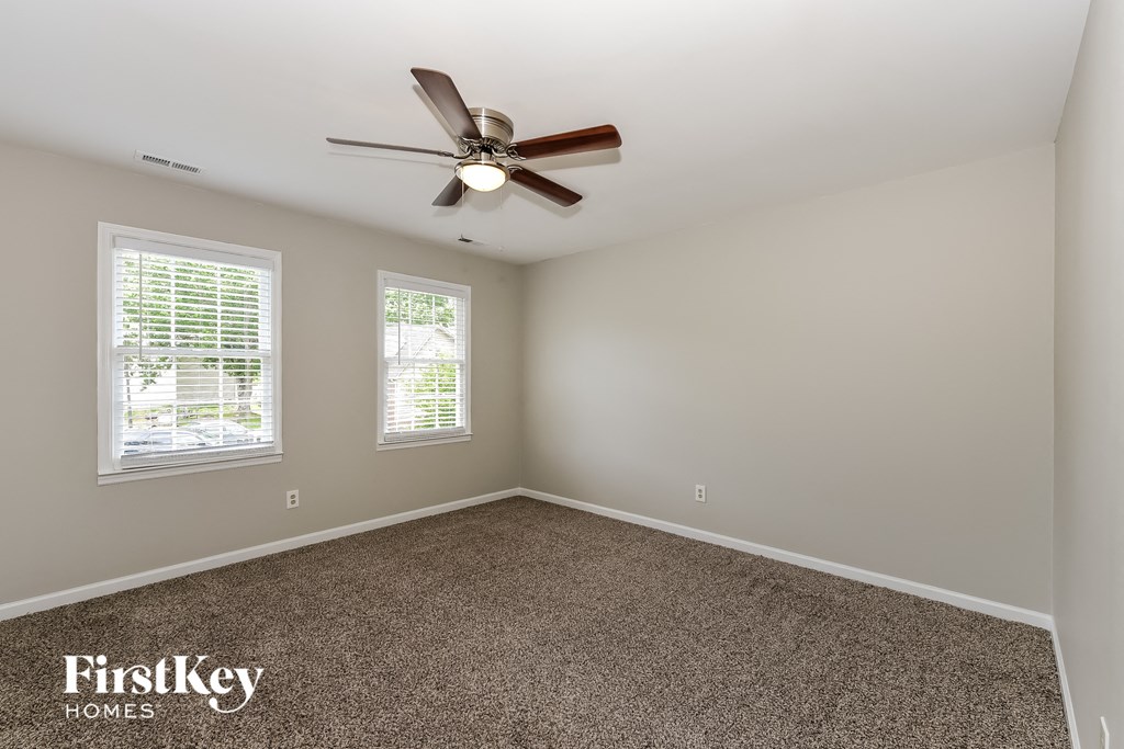 an empty room with a ceiling fan and two windows
