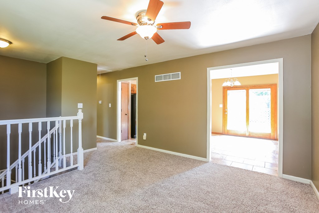 an empty living room with a ceiling fan and a staircase