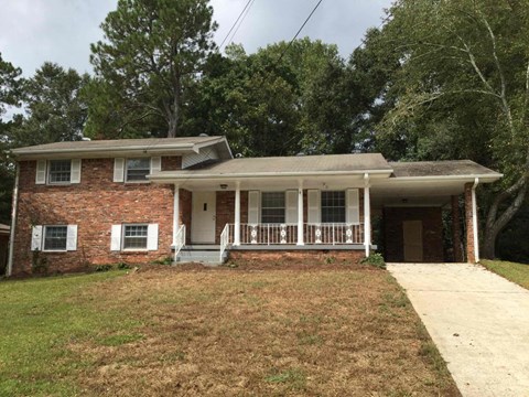 the front of a brick house with a porch and a driveway