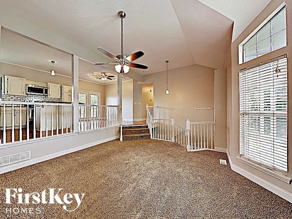 A spacious living room with a carpeted floor and a ceiling fan.