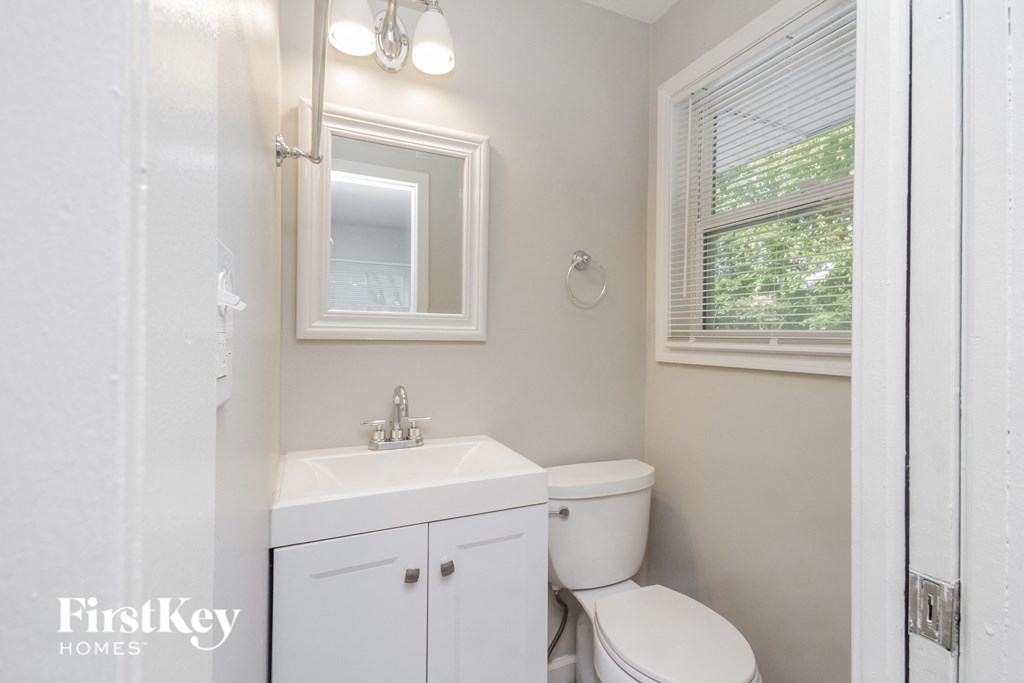 a white bathroom with a white sink and toilet and a window