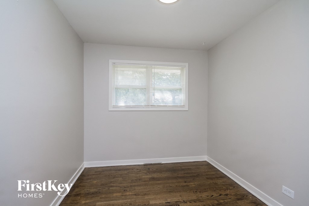 a bedroom with white walls and a wooden floor and a window