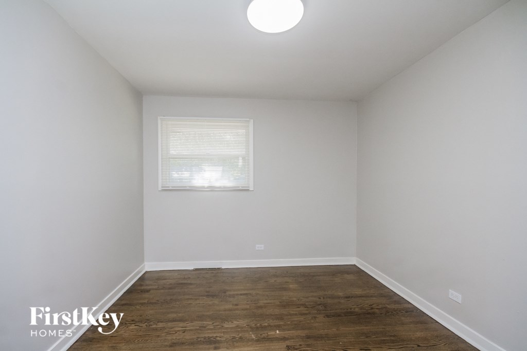a bedroom with white walls and wood floors and a window