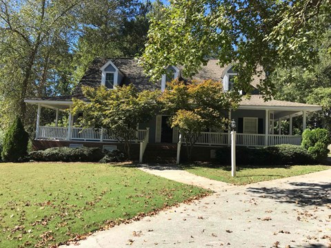 A house with a porch and a tree in front of it.