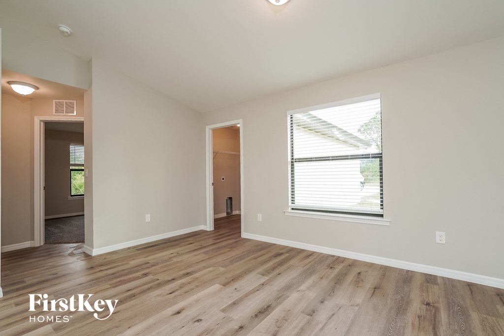A spacious room with wooden flooring and a window with blinds.