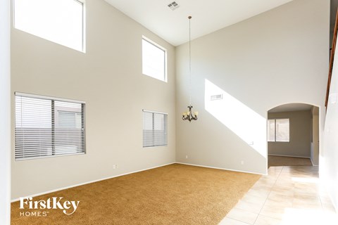 an empty living room with a rug and a hallway with windows