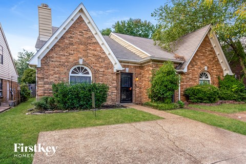 a small brick house with a driveway and grass