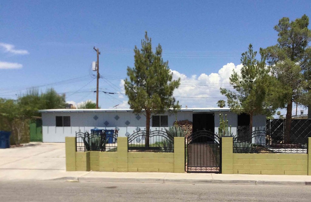 A white building with a black gate and a green trash can.