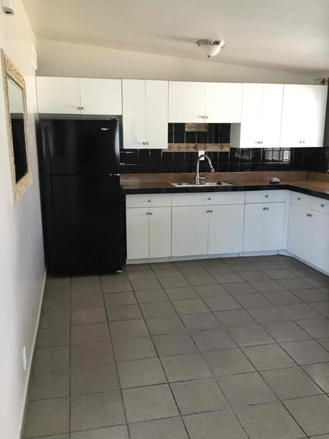 A black refrigerator sits in a kitchen with white cabinets.