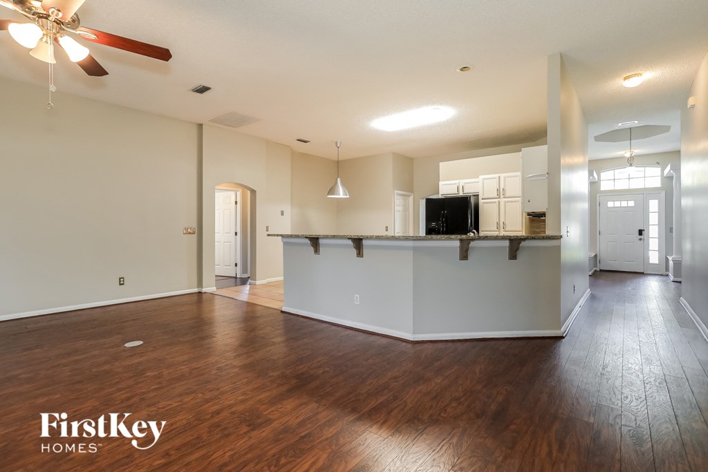 an empty living room with a kitchen and a ceiling fan