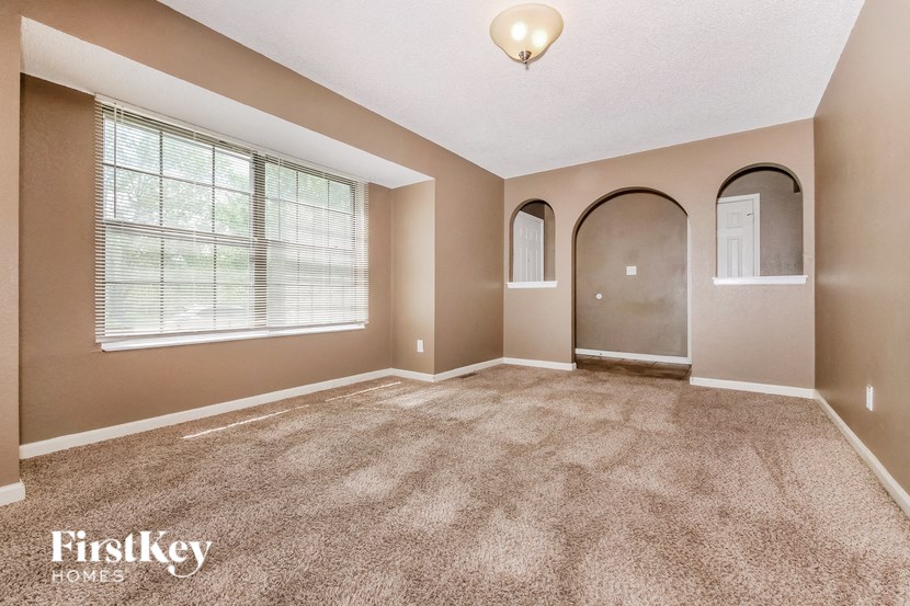 A spacious room with a carpeted floor and a large window with blinds.