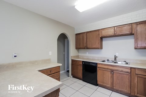 A kitchen with wooden cabinets and a black trash can.